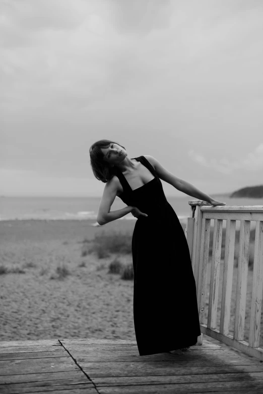 a black and white po of a woman in dress leaning on a fence