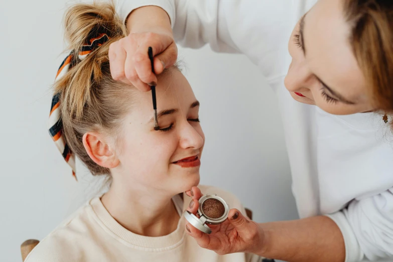 a woman has her hair done while another girl holds a piece of jewelry