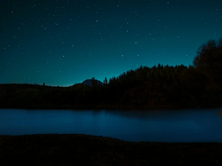 a lake near some trees is glowing up in the night