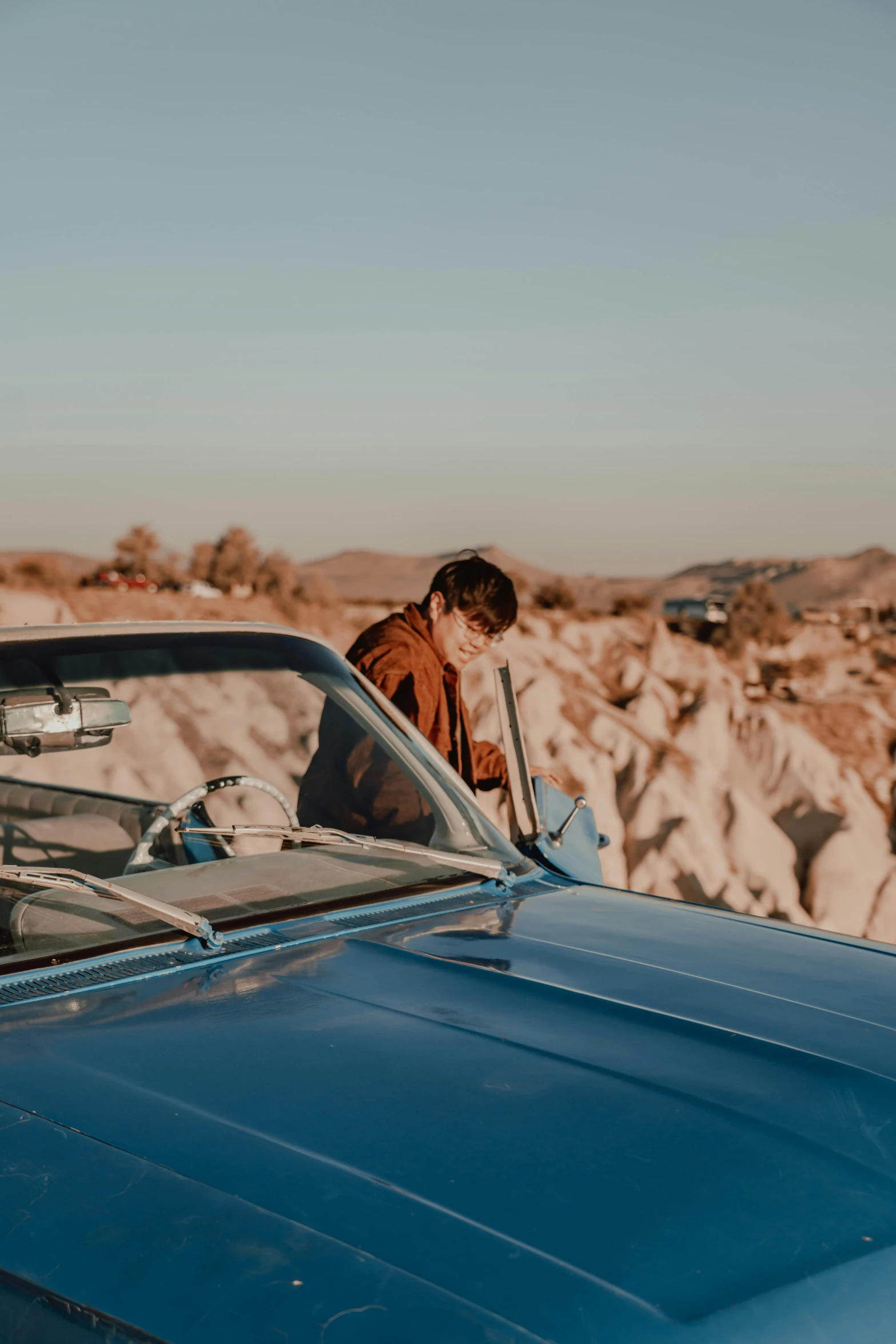 a man in a brown jacket is standing beside a car