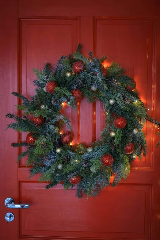 a wreath hangs on a red door decorated with lights