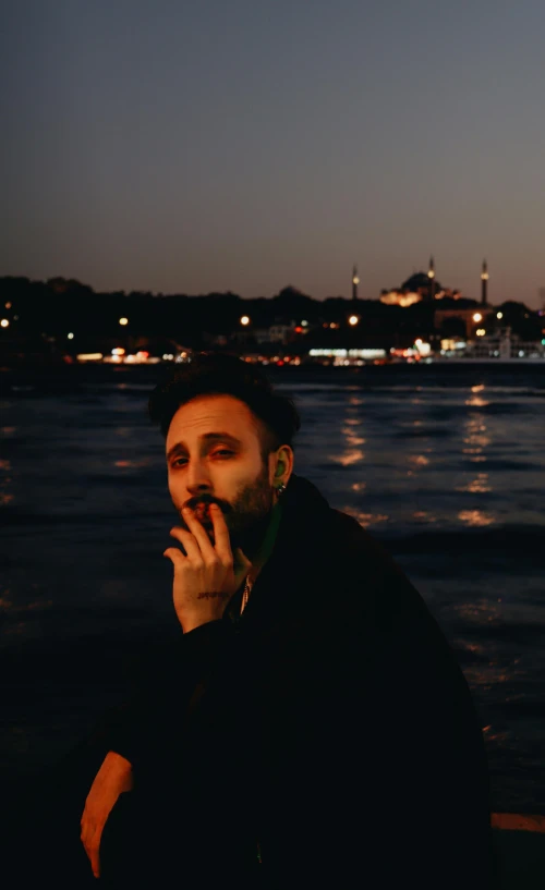 a man is sitting with his mouth open by the water