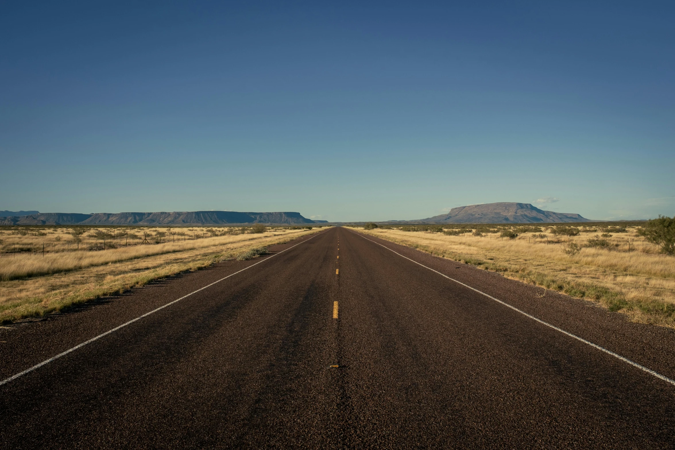 a black asphalt road is in front of some mountains