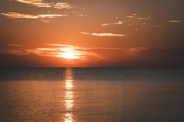 a bright, colorful sky rises above a calm sea as the sun reflects off in the water