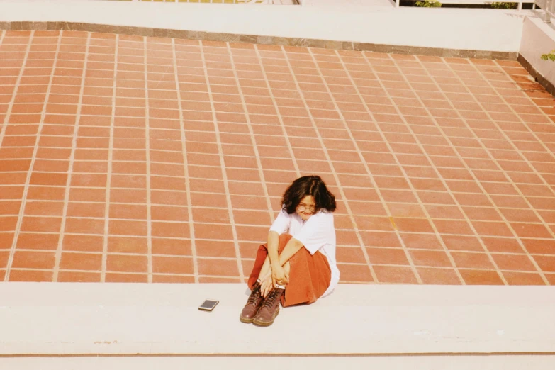 a young woman sitting on the side of a wall next to red brick