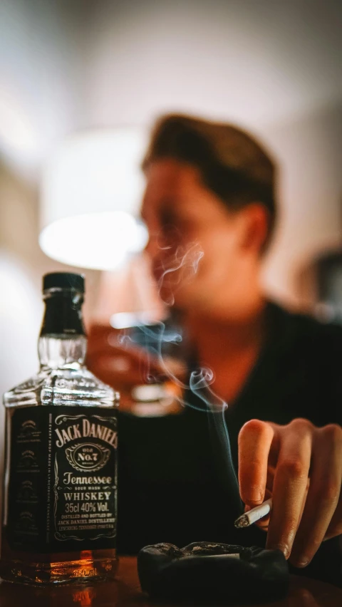 a man smoking a cigarette in front of a bottle of whiskey