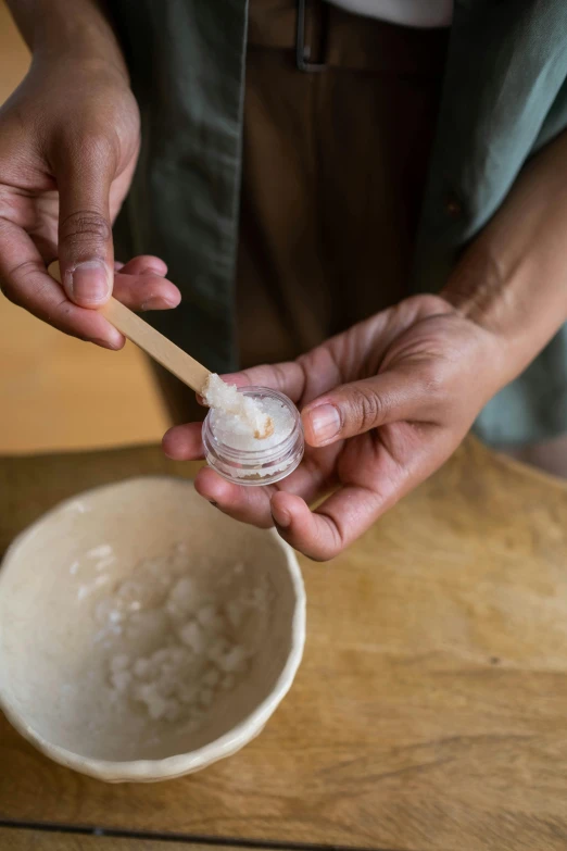 a man holding a container and spoon over a bowl