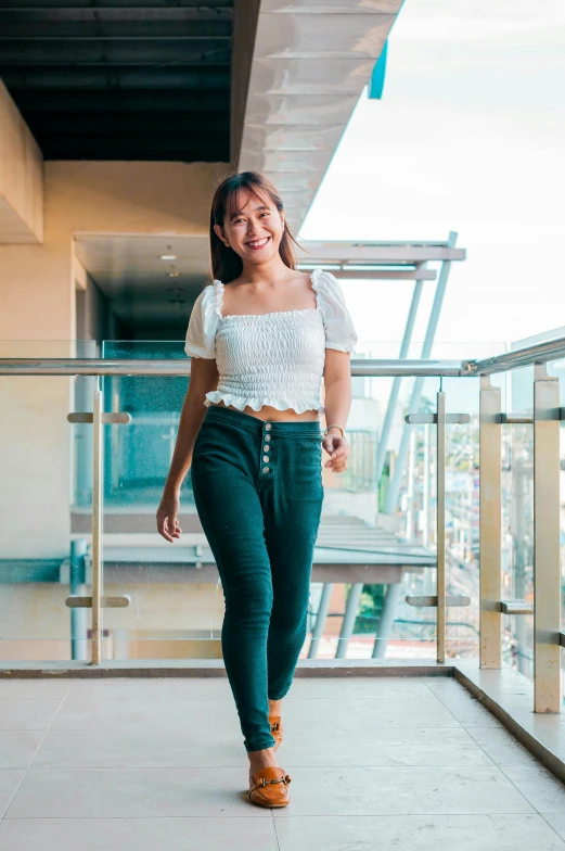 a smiling woman in green skinny jeans on a balcony