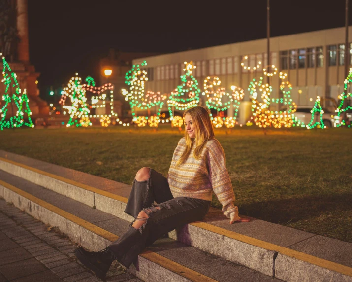 a person is sitting down on the stairs near christmas lights