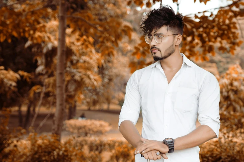 man in white shirt standing under trees with hands on hips