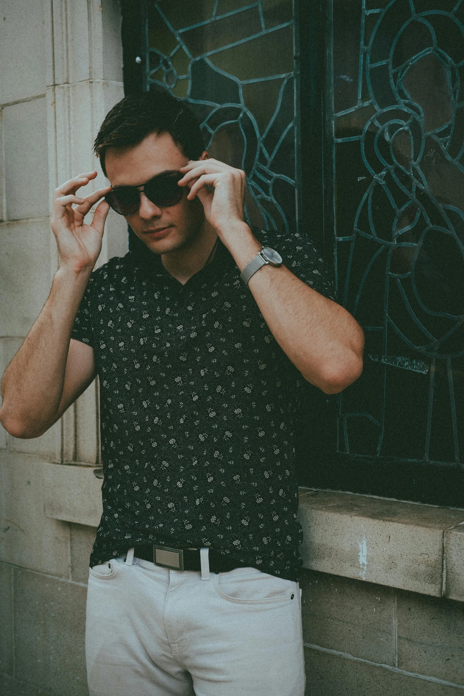 a man standing next to a wall wearing shades