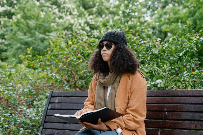 woman with glasses reading book while sitting on bench