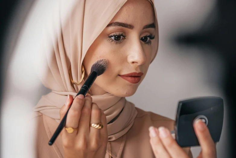 a beautiful young woman putting on makeup while holding up a brush