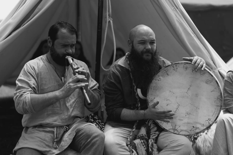 two men are sitting under a tent playing instruments