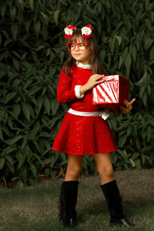 a little girl wearing glasses, a dress and a scarf holding a gift box