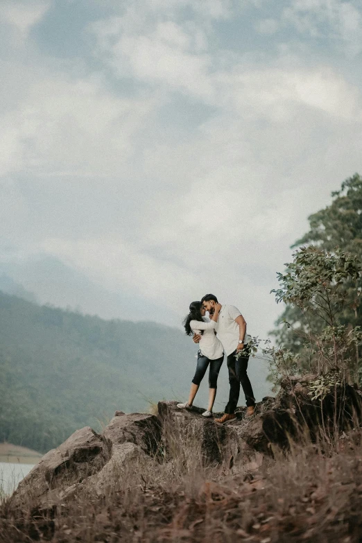the couple is hugging while standing on top of the mountain