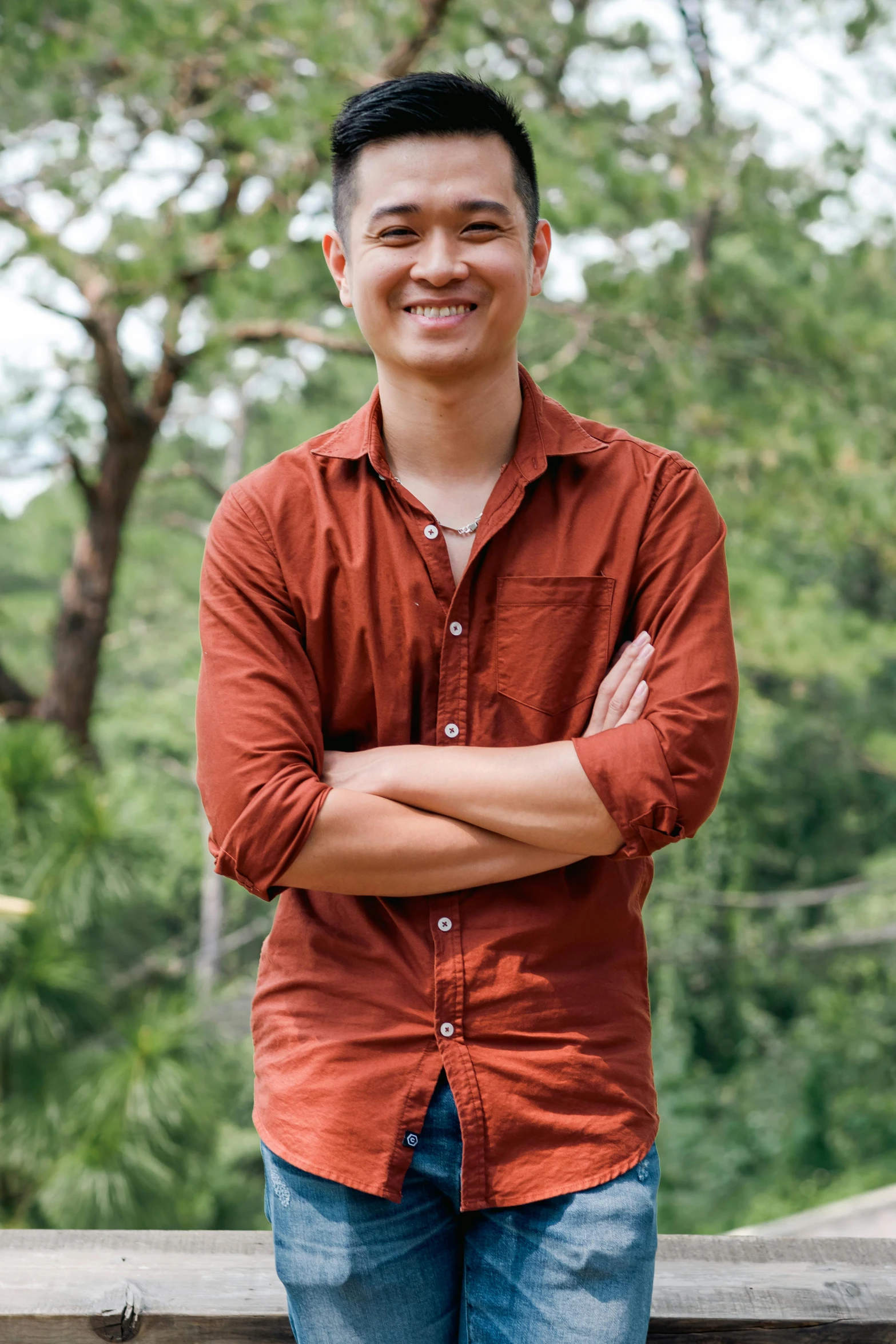 a man standing in front of some trees wearing a red shirt