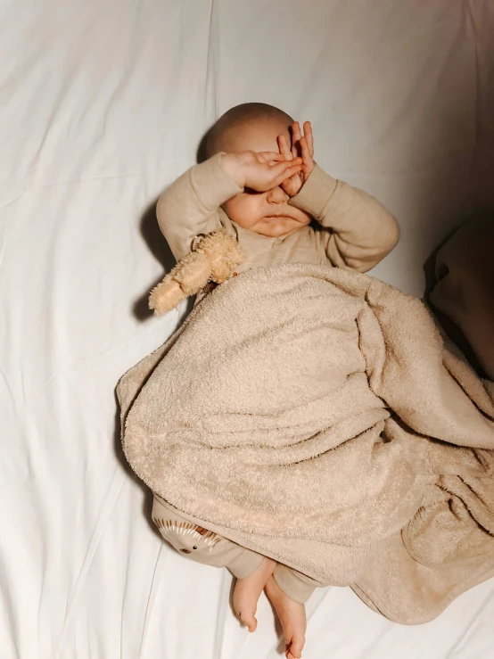 a baby covered with a blanket lying in bed