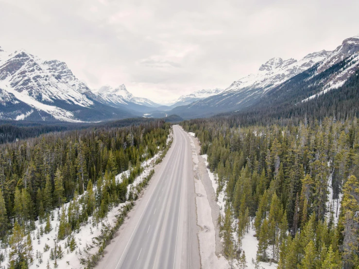 a car driving down an open road surrounded by snow and trees