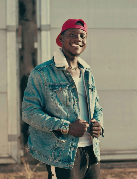 a man wearing a blue denim jacket, brown pants and a red hat