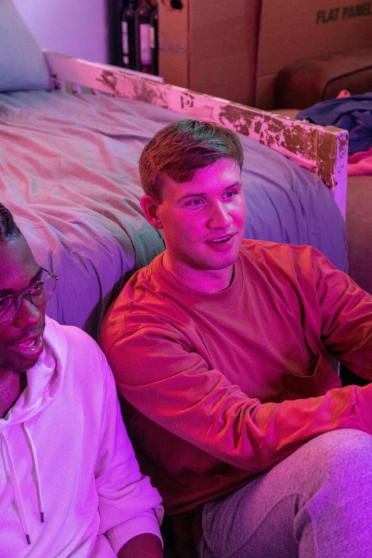 a man in a red and pink shirt sits next to another man