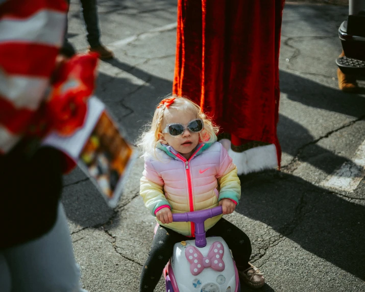 a little girl riding a toy bike wearing sunglasses