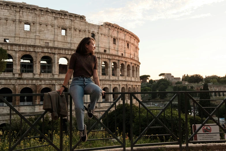 woman in jeans standing at the top of a stair railing near a roman collosion