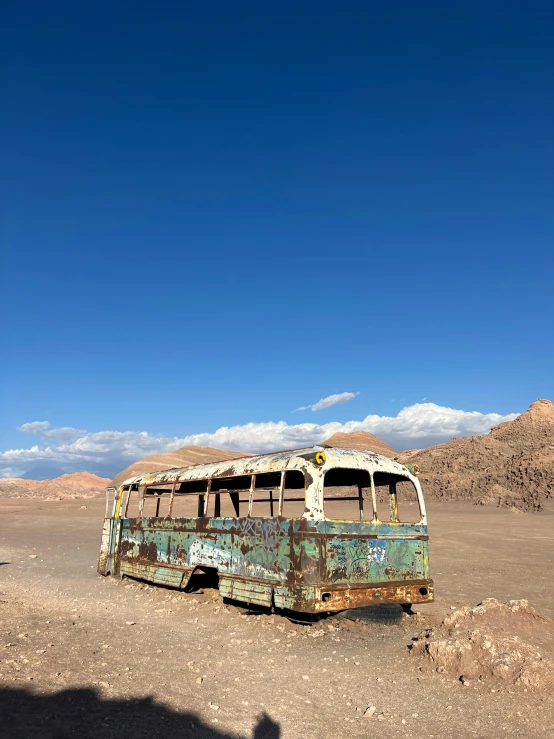 an old, rusty bus on the desert with a shadow cast by it