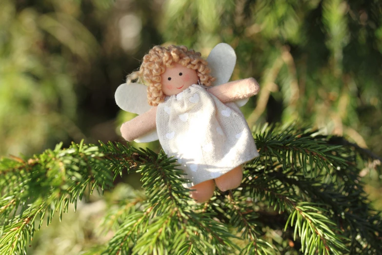 a pink angel decoration is hanging on a pine nch