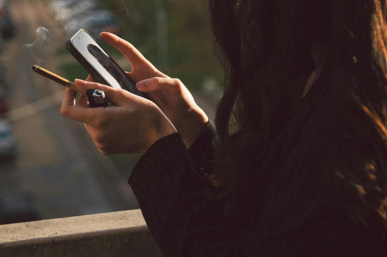 woman holding a cellphone, smoking, on the sidewalk