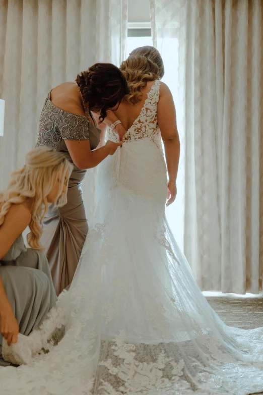 woman helping another woman adjust her dress on a bed