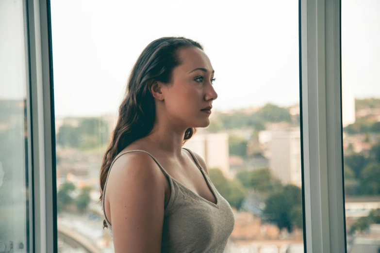 a young woman staring into a window overlooking a city