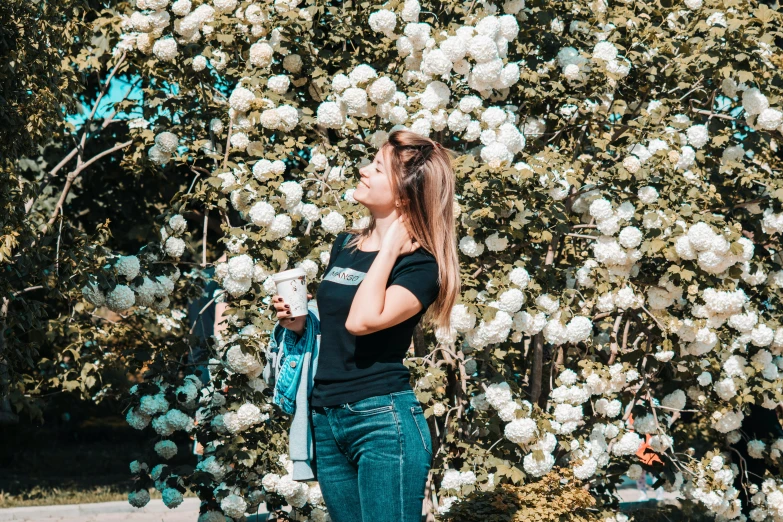 a young woman is smelling a large bush with many white flowers