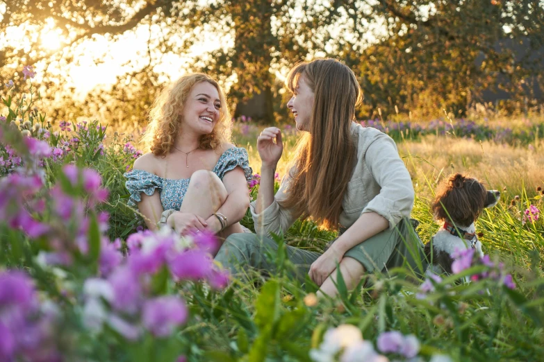 two girls sit on the grass in front of a field of flowers