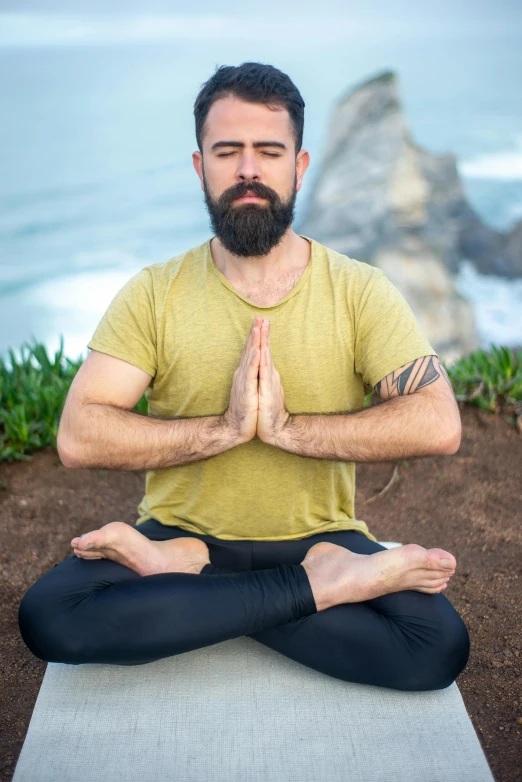 bearded man meditating on rug next to ocean