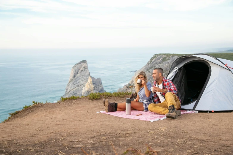 two people sit outside of a tent on top of a cliff