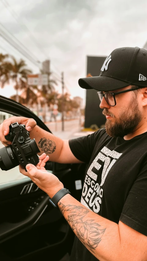 a man wearing glasses and a black t - shirt takes a picture in a car