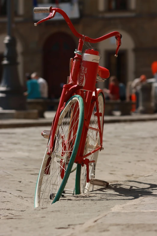 a red bike with two green spokes sitting on a cobble stone walkway