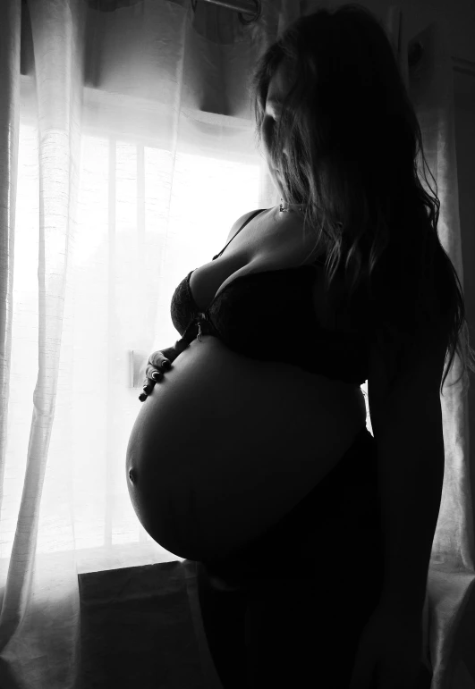 pregnant woman in dark room standing beside a window