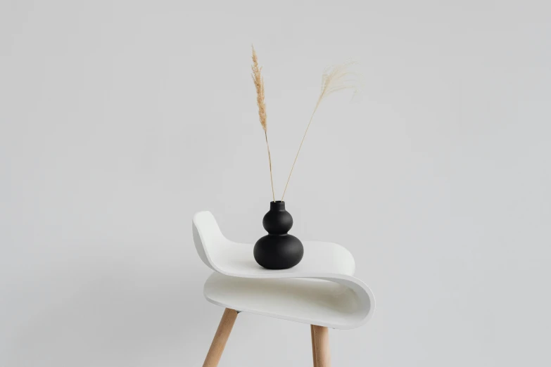 a black vase and a brown stick on the edge of a white chair