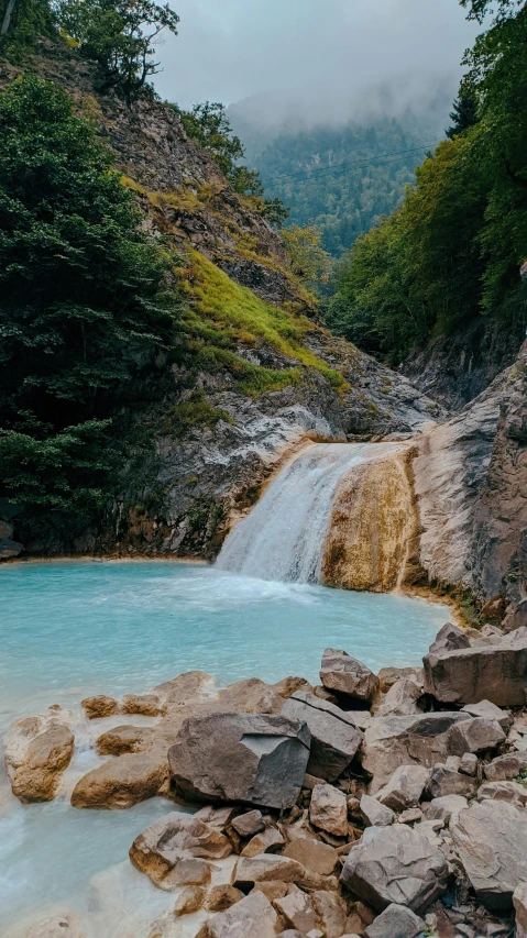 waterfall in a pool with trees and a mountain