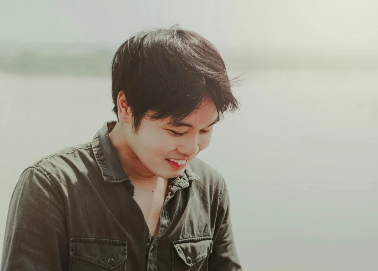 a man smiles as he stands by the lake