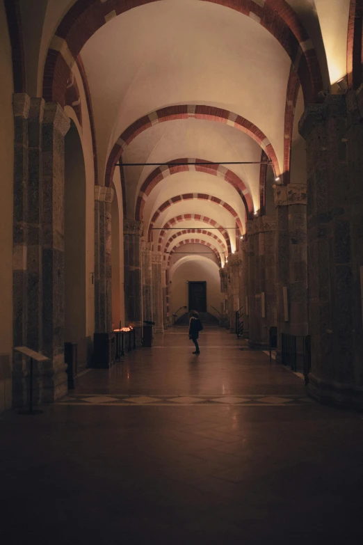 a man walking down an empty hall with red arches