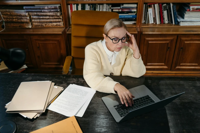 a woman in glasses with laptop and a book on a table