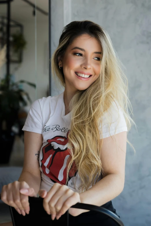 a woman in a white t - shirt smiles while sitting down