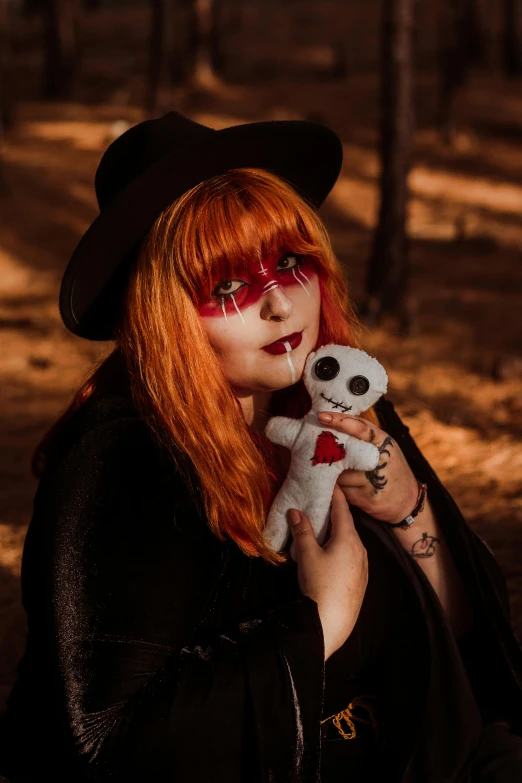 a red haired woman with face paint sitting on ground holding a stuffed toy