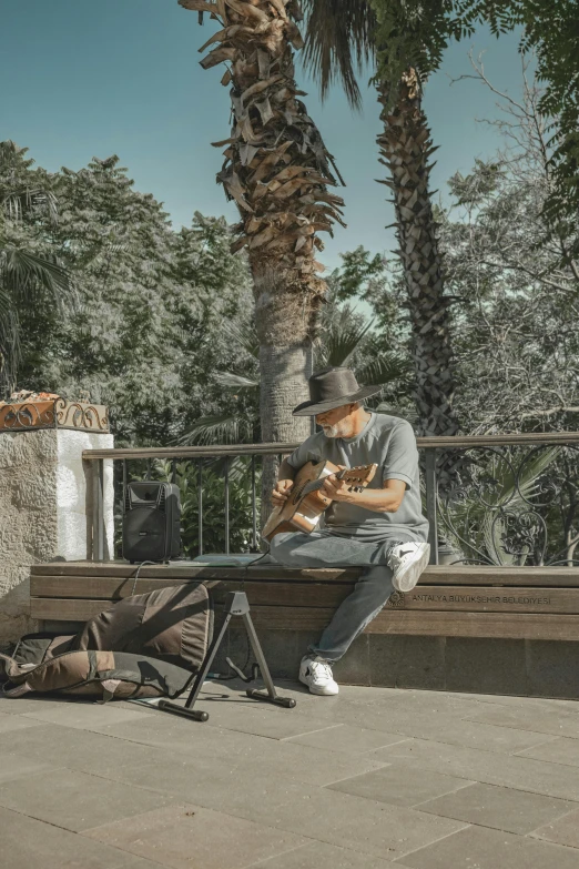 man in fedora sitting on a park bench playing the ukeler