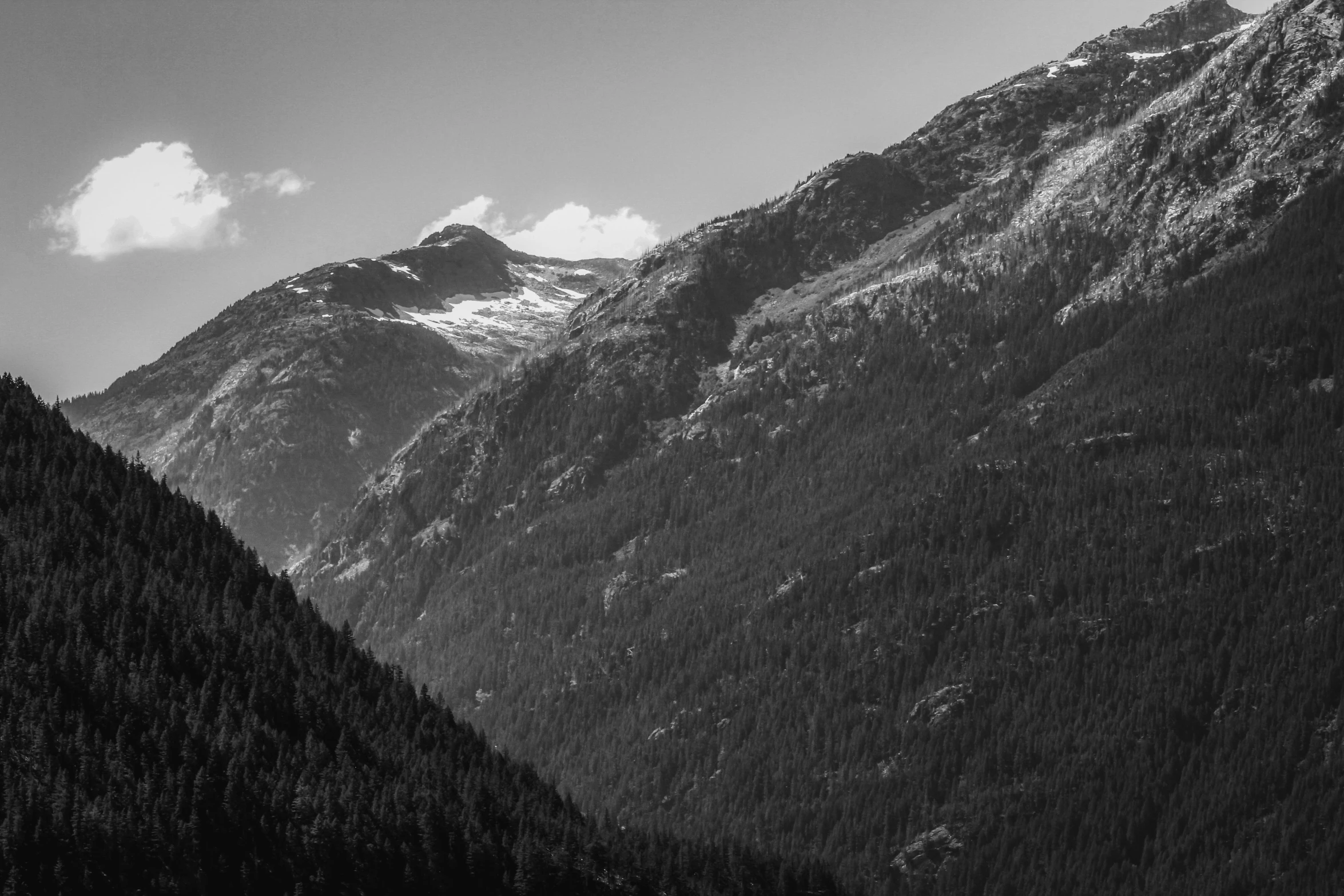 mountains surrounding a river and forest line with clouds