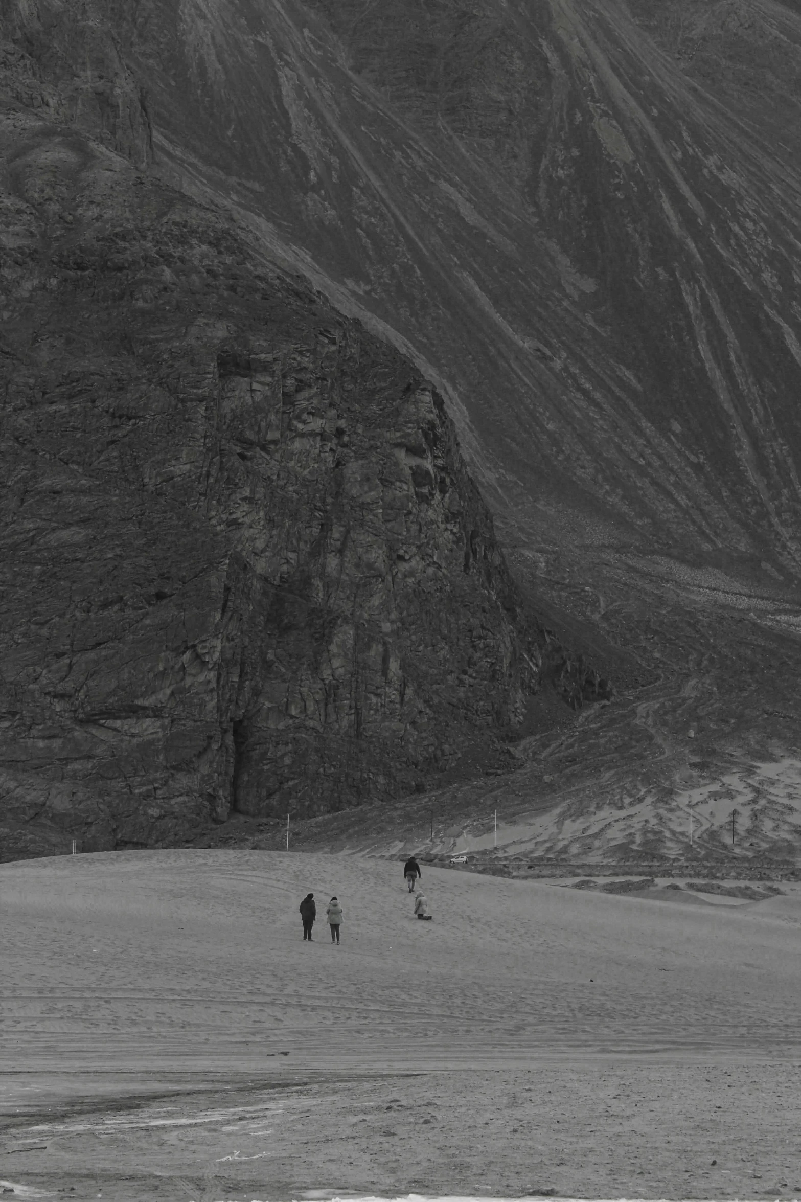 three men walking on sand near large rocky mountains