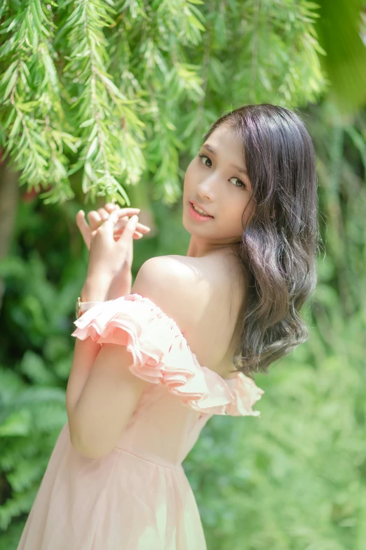 a young woman in a pink dress is standing by some trees